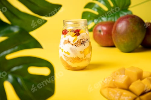 Preview: A healty breakfast with mango, yogurt and granola on a yellow background with leaves and mango