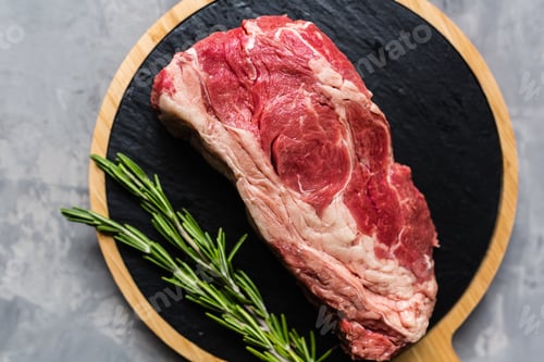 Preview: Flat lay of raw beef on cutting plate with rosemary on gray concrete background
