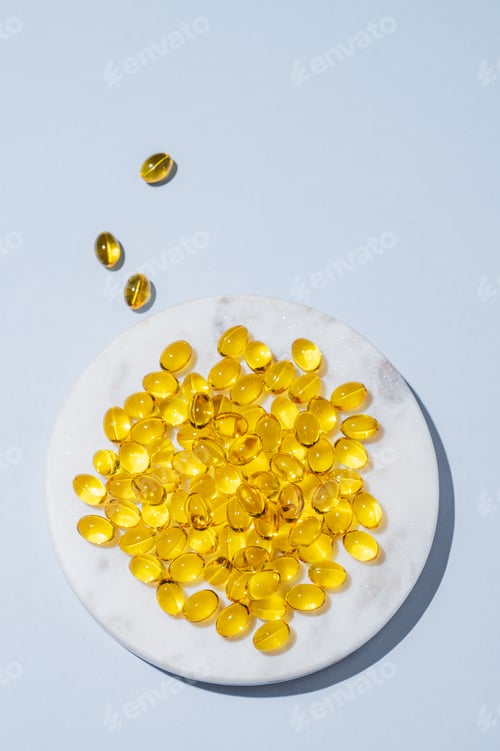 Preview: Yellow softgel vitamins capsules on a white marble plate on a blue background with shadow