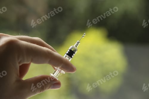 Preview: Closeup shot of a female holding a syringe, on a blurred background