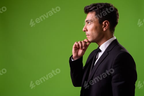 Preview: Young handsome Hispanic businessman against green background