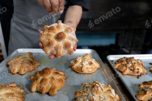 Preview: A young Hispanic baker is covering a Day of the Dead bread with sugar