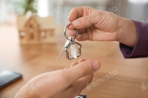 Preview: Real estate agent giving key with trinket to client in office, closeup