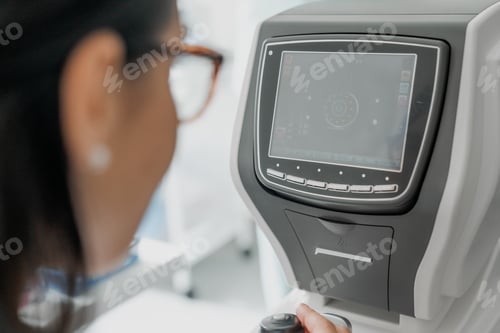 Preview: Close up shot of female doctor working on auto refractometer while checking eyes in medical clinic