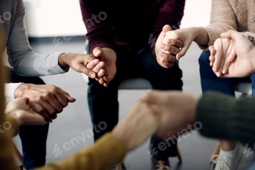 Preview: Close-up of group of people holding hands during psychotherapy session.