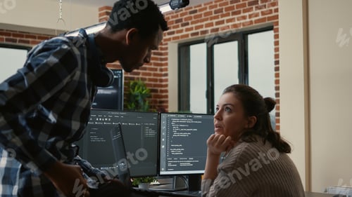 Preview: Junior developer sitting down on desk showing laptop with source code to senior dev
