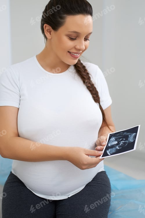 Preview: Attractive woman looking at ultrasound photos at clinic