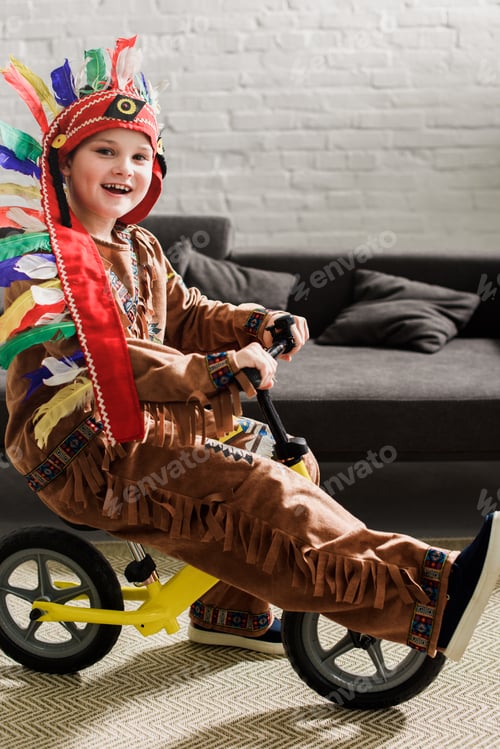 Preview: happy little boy in indigenous costume on runbike playing at home