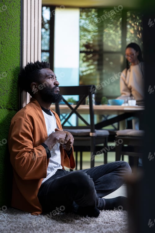 Preview: Black man, depressed and unwell, sitting alone, on the floor at home