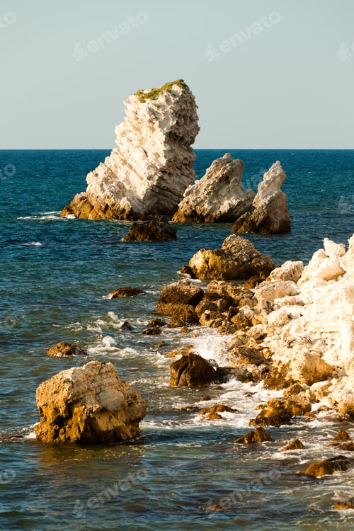 Preview: Seascape of still blue sea waters shore, rocky coastline and bright sun