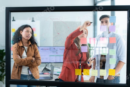 Preview: Multiethnic young business people brainstorming on a project by writing on the glass wall