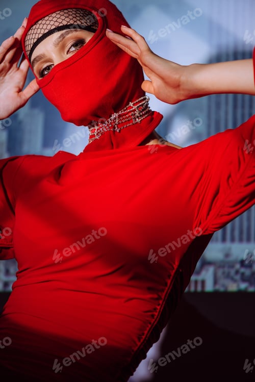 Preview: stylish woman in red dress and balaclava on city background