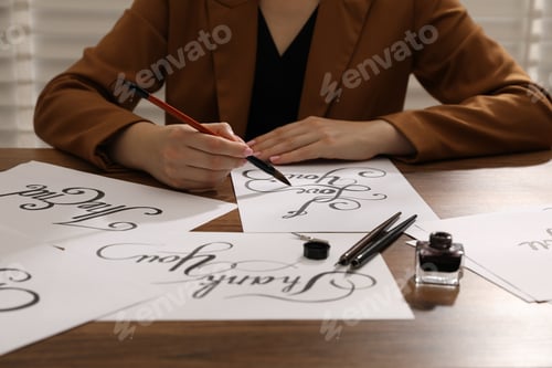 Preview: Calligraphy. Woman with brush writing phrase I Love You on sheet of paper at wooden table, closeup