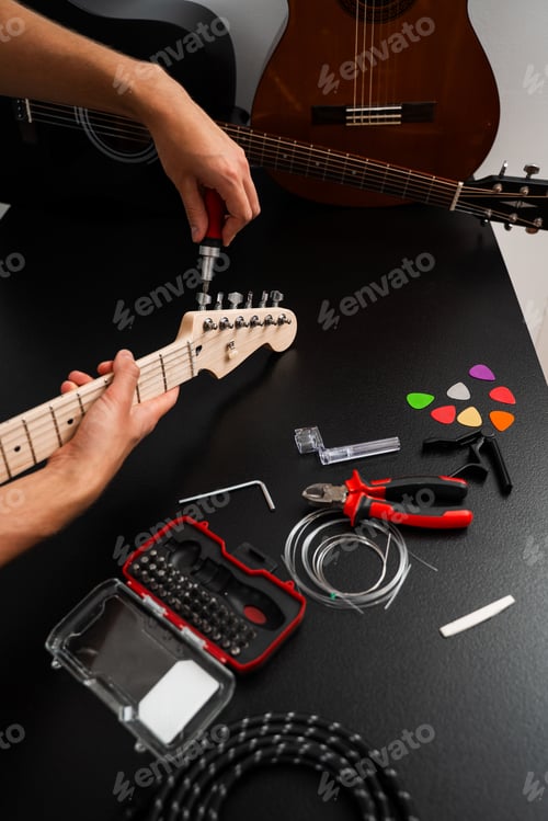 Preview: Musician tightening tuning pegs on guitar headstock with tools