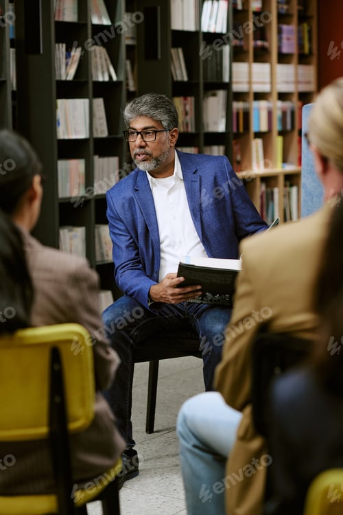 Preview: Middle Aged South Asian Man Giving Presentation with Book to Diverse Audience