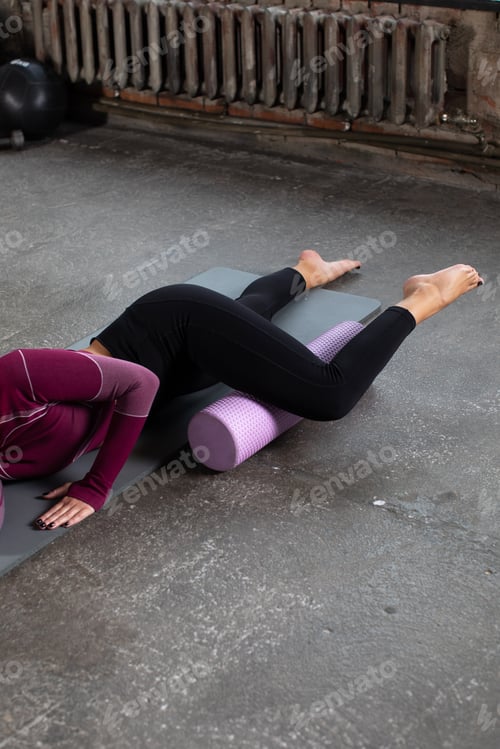 Preview: A young woman in sportswear performs a myofascial hip massage with a roller. Muscle recovery, mfr.