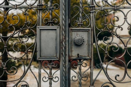Preview: Forged doors leading into a charming European garden, showcasing vintage architectural design.