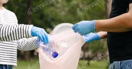 Preview: Two people keeping garbage plastic bottle into black bag at park.Clearing, pollution, ecology