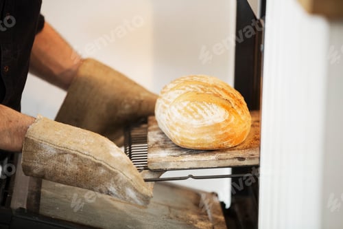 Preview: Close up of a baker taking a freshly baked loaf bread out of an oven.