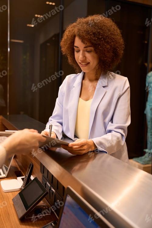 Preview: African woman filling out registration form at front desk