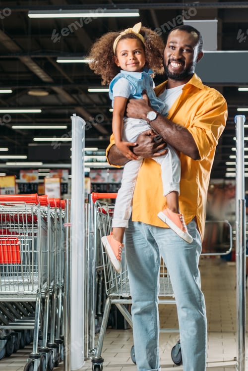 Preview: smiling african american man embracing and holding little daughter in supermarket