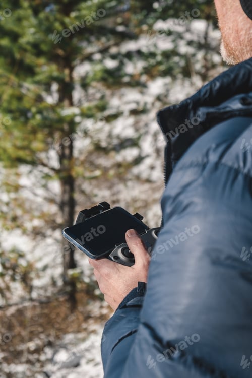 Preview: A man holds a remote control in his hands and controls a drone in the winter in the forest. Close-up