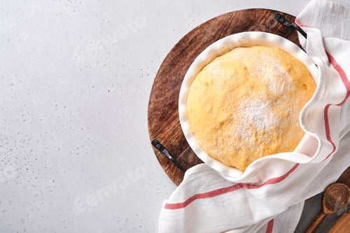Preview: Raw yeast dough with pumpkin in white bowl covered with towel on the floured kitchen table, recipe i
