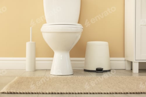 Preview: Toilet bowl, brush and trash bin near beige wall in restroom