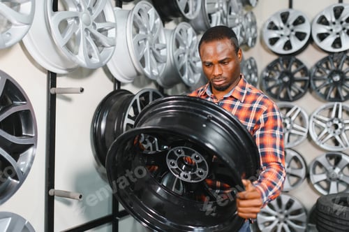 Preview: African american Car mechanic holding car rims ready to mount the wheels in workshop