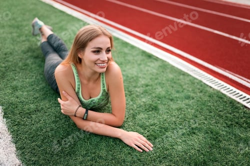 Preview: Fitness girl lying on the grass of a football field