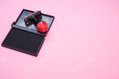 Preview: Black ink pad with a rubber stamp isolated on pink background