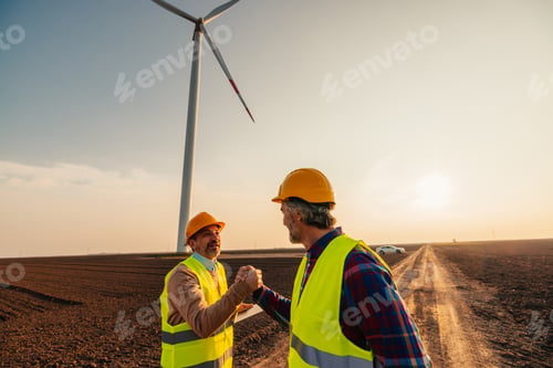 Preview: Colleagues shaking hands with wind turbines on background