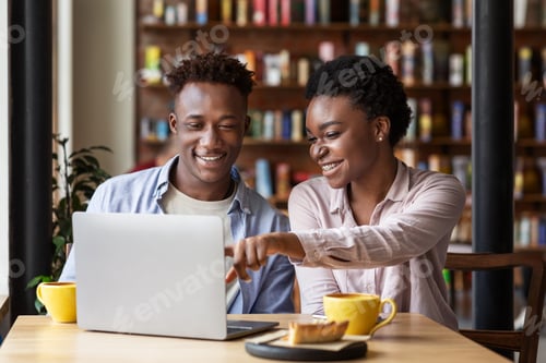 Preview: Cheerful black girl with her boyfriend watching movies together on laptop at cafe