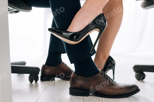 Preview: cropped view of secretary in heels touching leg of businessman in office