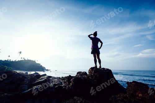 Preview: Strong woman looking at the sunrise landscape on seaside rock cliff edge