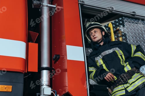 Preview: low angle view of firefighter in helmet looking away at fire department