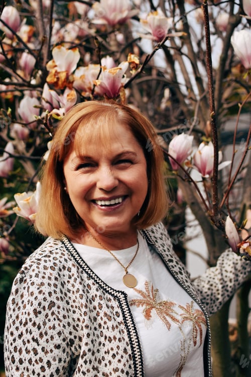 Preview: Portrait of smiling senior woman next to magnolia tree