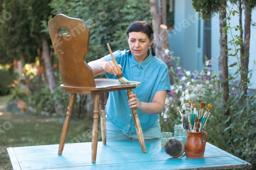 Preview: Woman painting a wooden furniture outdoors, an eco-friendly re-use business.