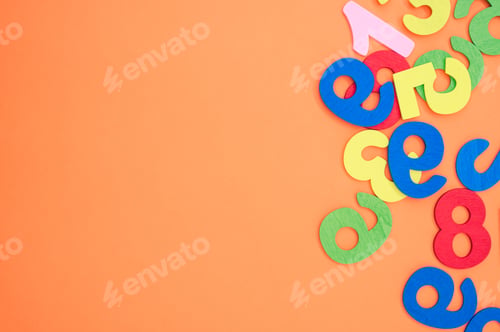 Preview: Flat lay of colorful wooden numbers scattered on an orange surface - space for text