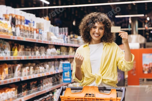 Preview: Woman pushing shopping cart and showing fidelity card in supermarket