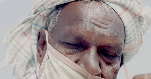 Preview: Closeup of an old South Asian man's face trying to put on a Covid mask with his eyes closed