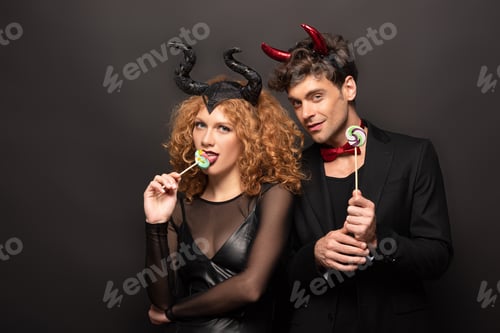 Preview: sexy couple in halloween costumes eating lollipops on black