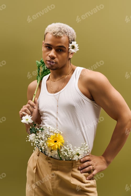 Preview: Young man in trendy tank top holds flowers with style in a vibrant studio setting