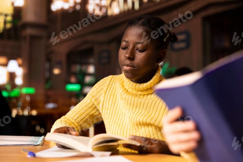 Preview: Black schoolgirl studying in a public library reading required literature