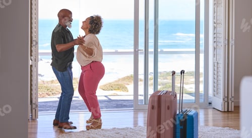 Preview: Mature Couple With Luggage Dancing In Beachfront House Overlooking Ocean For Summer Vacation