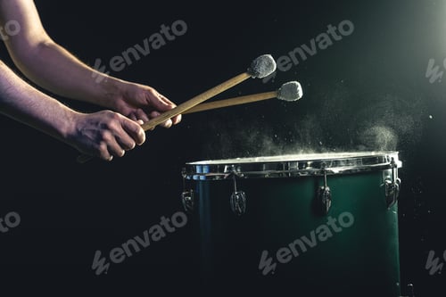 Preview: A man plays a musical percussion instrument with sticks on a dark background.