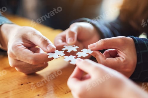 Preview: Closeup image of a group of people holding and putting a piece of white jigsaw puzzle together