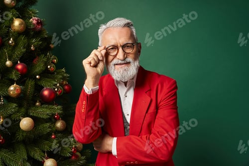 Preview: classy man dressed as Santa crossing arms and touching glasses next to fir tree, winter concept
