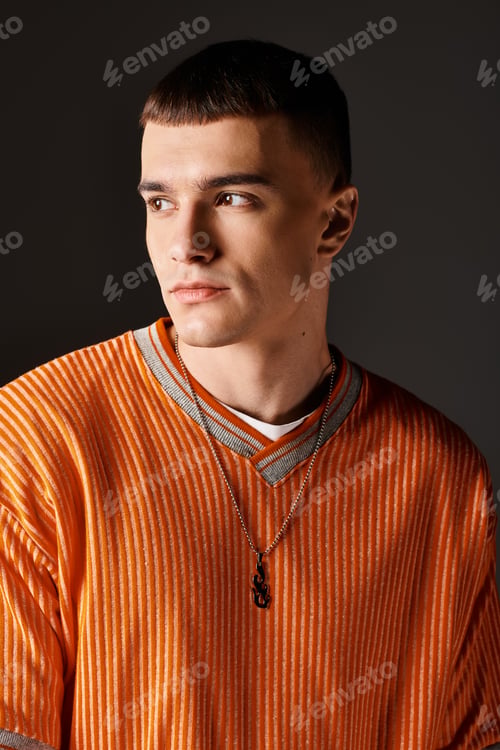 Preview: Fashion portrait of stylish handsome man in orange jumper looking away on grey background