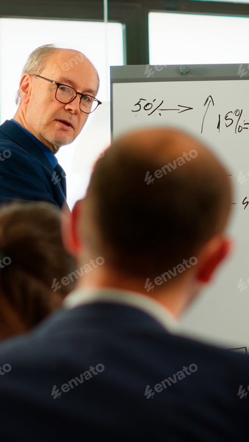 Preview: Elderly businessman giving presentation to multiethnic team using flip chart